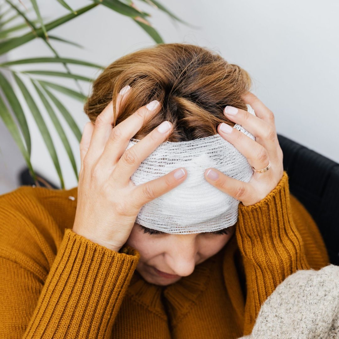 Woman with head injury holding her head in pain indoors.
