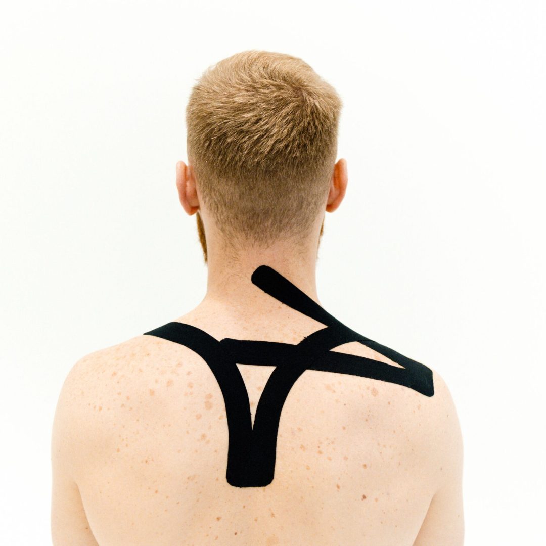 A man with kinesiology tape applied on shoulders. Back view against white background.