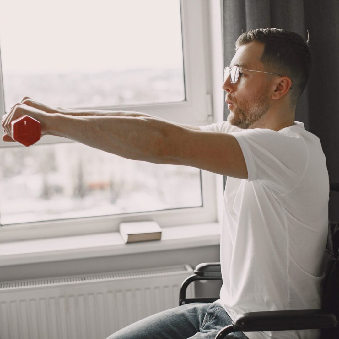 A man in a wheelchair exercising with a dumbbell by a bright window, promoting inclusivity and health.